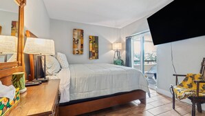 Een slaapkamer met een bed, nachtlampjes, een houten dressoir, een spiegel en een aan de muur bevestigde televisie.