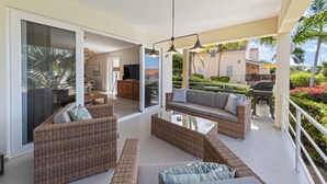 Une vaste terrasse dotée de meubles en osier, une porte vitrée donnant sur un espace intérieur et une vue sur un jardin.