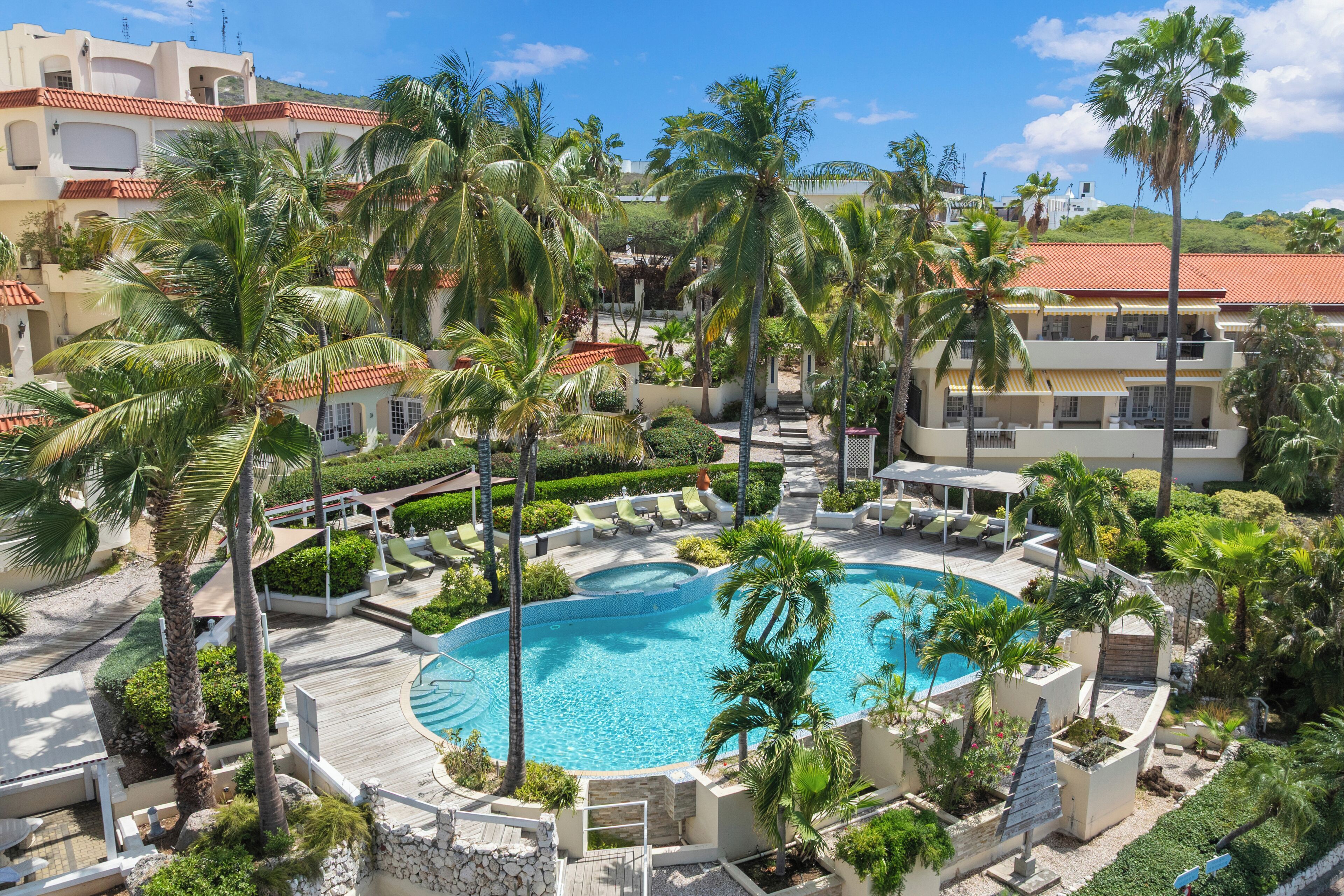 Un resort con piscina central, palmeras y montañas al fondo.