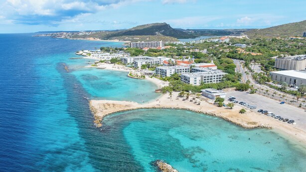 Une station balnéaire dotée de propriétés en bord de mer, d’eaux turquoise cristallines et d’un paysage vallonné en arrière-plan.