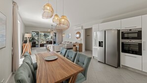 Une cuisine moderne dotée d’appareils électroménagers en acier inoxydable, un coin repas avec une table en bois et des chaises à revêtement vert, ainsi qu’un éclairage suspendu.