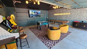 A room with a foosball table, two yellow armchairs, a sofa, a TV, and a wall with a pattern. - The Funky Fun Haus - Pickleball, Hot Tub, Arcade (Columbus)