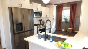 A modern kitchen with stainless steel appliances, white cabinetry, and a central island with a sink and soap dispenser. - The Funky Fun Haus - Pickleball, Hot Tub, Arcade (Columbus)