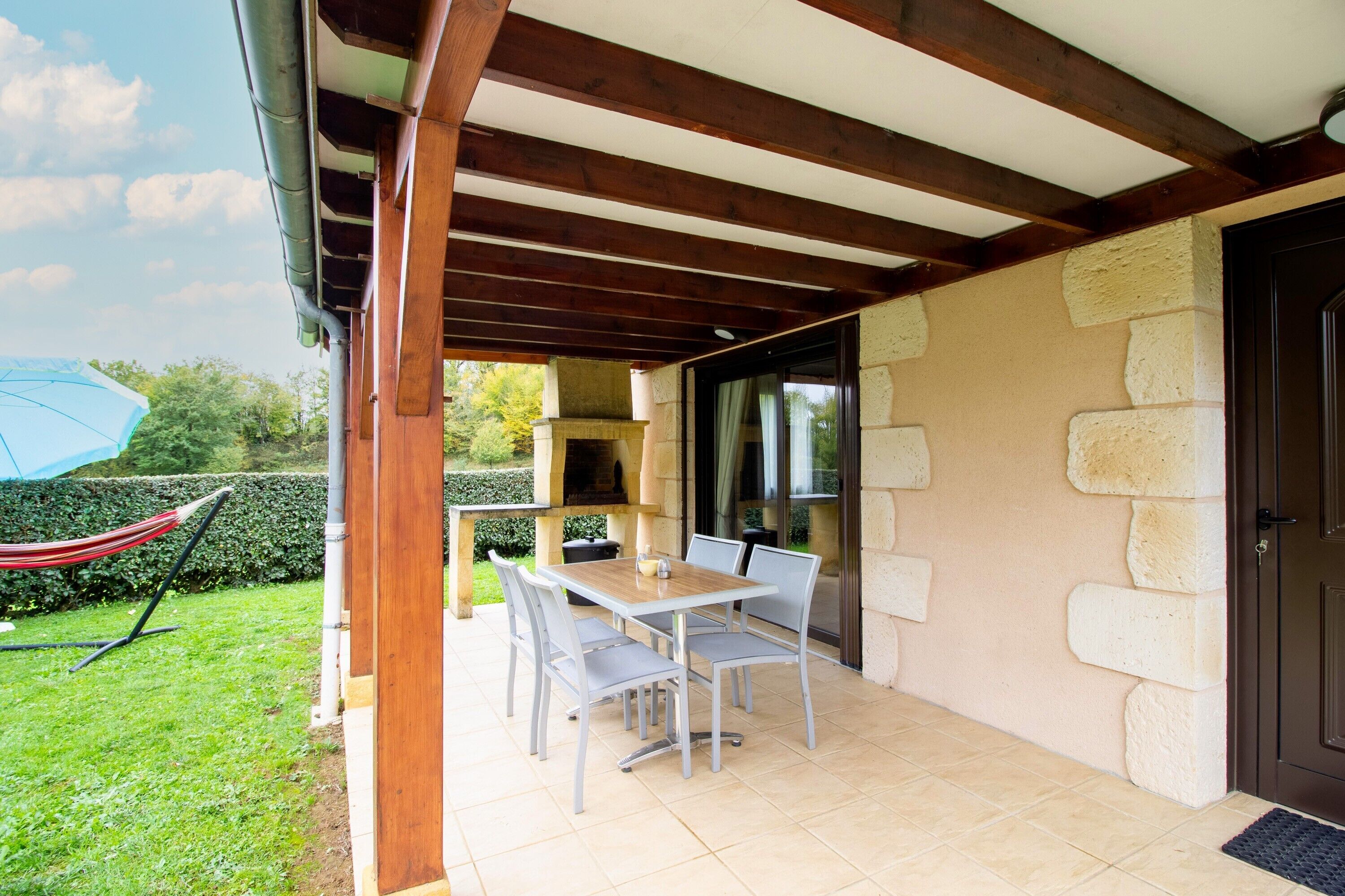 An outdoor patio with a table and chairs, a hammock, and a stone wall.