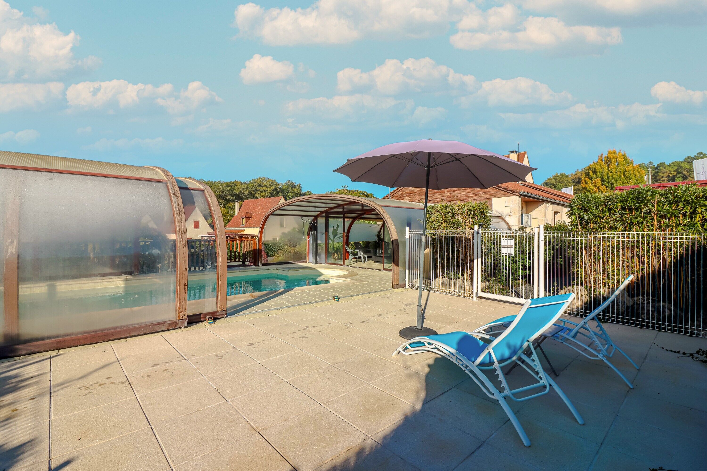 Une piscine entourée de parois en verre, des chaises longues et une pergola avec un parasol.