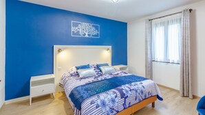 A bedroom with a bed, bedside tables, a nightstand, a wall-mounted light fixture, and a window with curtains. - Holiday Home 'Maison Tournesol' with Shared Pool, Wi-Fi and Air Conditioning (Castelnaud-la-Chapelle)