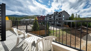 Ein Balkon mit zwei weißen Stühlen und Blick auf eine Wohngegend mit Gebäuden und Bäumen, der unter einem bewölkten Himmel liegt.