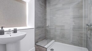 Un baño moderno con un lavabo blanco, cabina de ducha de vidrio y ventana.