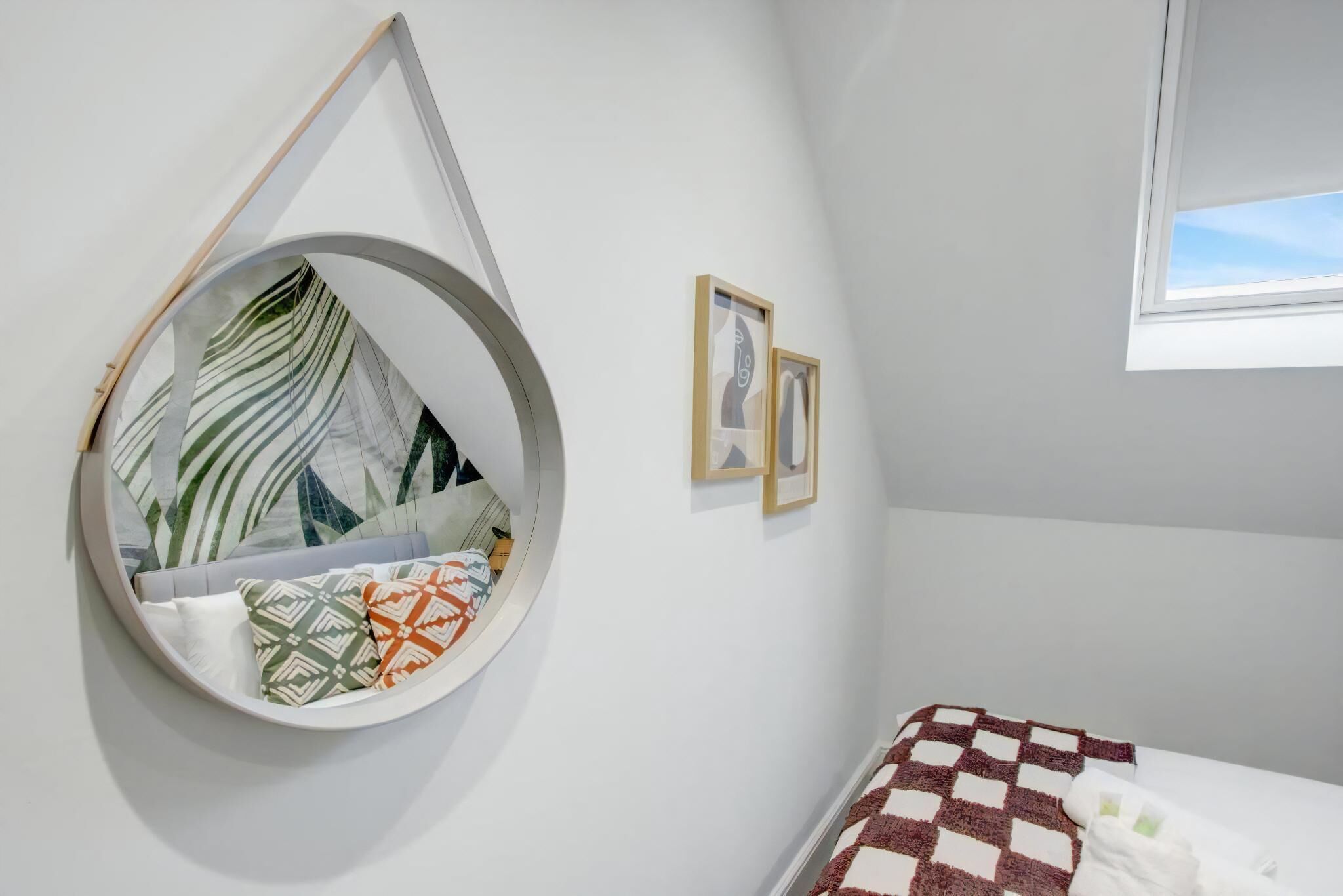 Un fauteuil suspendu de forme circulaire, agrémenté de coussins à motifs, un lit recouvert d’une couverture à carreaux et deux tableaux encadrés accrochés au mur.