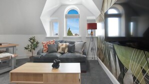 Una sala de estar moderna con un sofá gris, una mesa de centro de madera y un televisor montado en la pared.