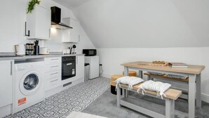 Cocina compacta con lavadora, microondas y comedor con mesa y bancos.