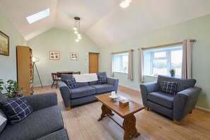 A spacious living room with two grey sofas, a wooden coffee table, and a dining area with a table and chairs. - Host & Stay | The Byres (Dipton)