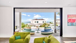 A modern living room with two green sofas, a coffee table, and a view of a beach and mountain in the background.