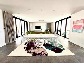 A modern living room with a large glass door, a green sofa, a white coffee table, and a colorful rug. - Villa Jupiter - Oceanview with Private Pool (Providenciales)