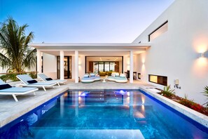 A modern pool area with lounge chairs and a seating area, surrounded by a white building with large windows and outdoor lighting. - Villa Jupiter - Oceanview with Private Pool (Providenciales)
