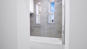 Un baño moderno con bañera, dos ventanas y paredes cubiertas de azulejos grises.