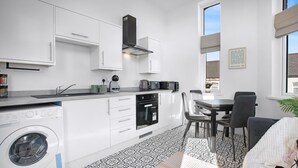 Una cocina moderna con armarios blancos, lavadora integrada y comedor con mesa y sillas.