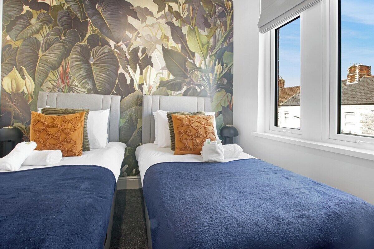 A hotel room with two beds, a large window, and a tropical leaf mural on the wall.