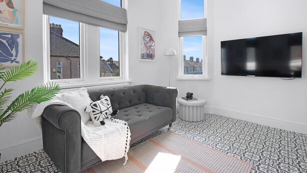 Una sala de estar moderna con un sofá gris, un televisor de pantalla plana y ventanas amplias.