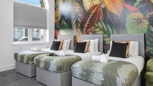 Une chambre d’hôtel avec trois lits, une grande fenêtre et un mur décoré d’un motif de feuilles aux couleurs vives.