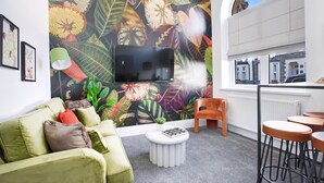 A living room with a large TV, a green sofa, a round white coffee table, and a vibrant floral mural on the wall. - Stadium View Family & Group 3-bed Retreat (Cardiff)