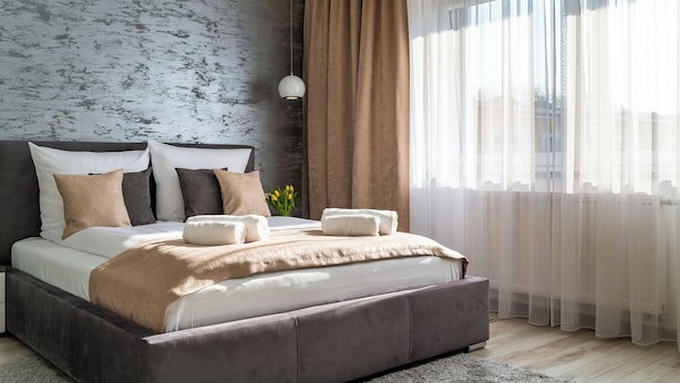 A modern bedroom with a large bed, a grey textured wall, a hanging light, and sheer curtains. - Panorama Park (Świnoujście)
