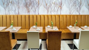 A restaurant with booths and tables, each with a white cup and saucer, and a vase with a yellow flower. - Panorama Park (Świnoujście)