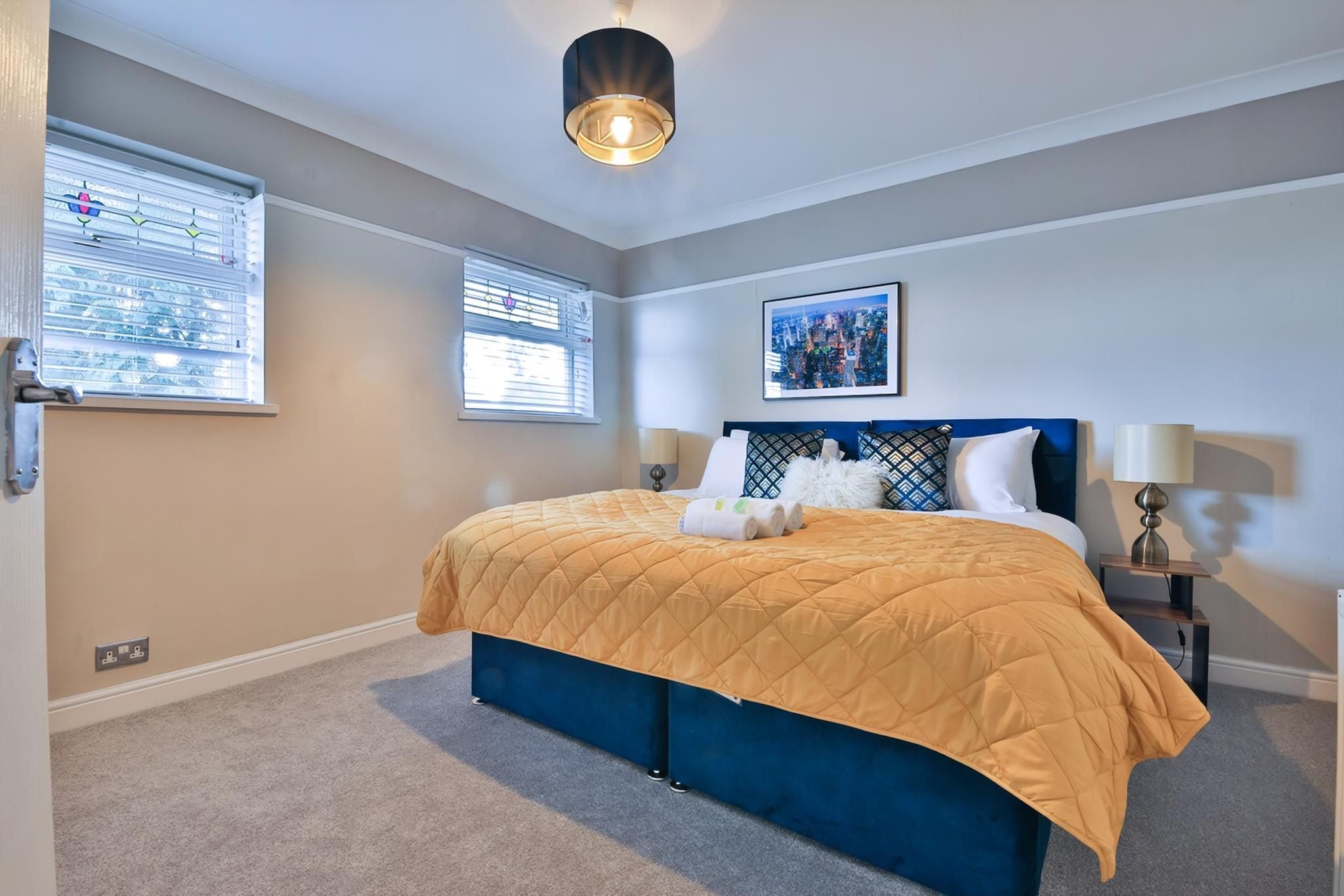 A bedroom with a bed, two bedside tables, a wall-mounted artwork, and a ceiling light fixture.