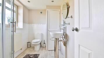 A bathroom with a toilet, sink, mirror, and a glass shower enclosure.