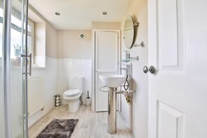 A bathroom with a toilet, sink, mirror, and a glass shower enclosure.