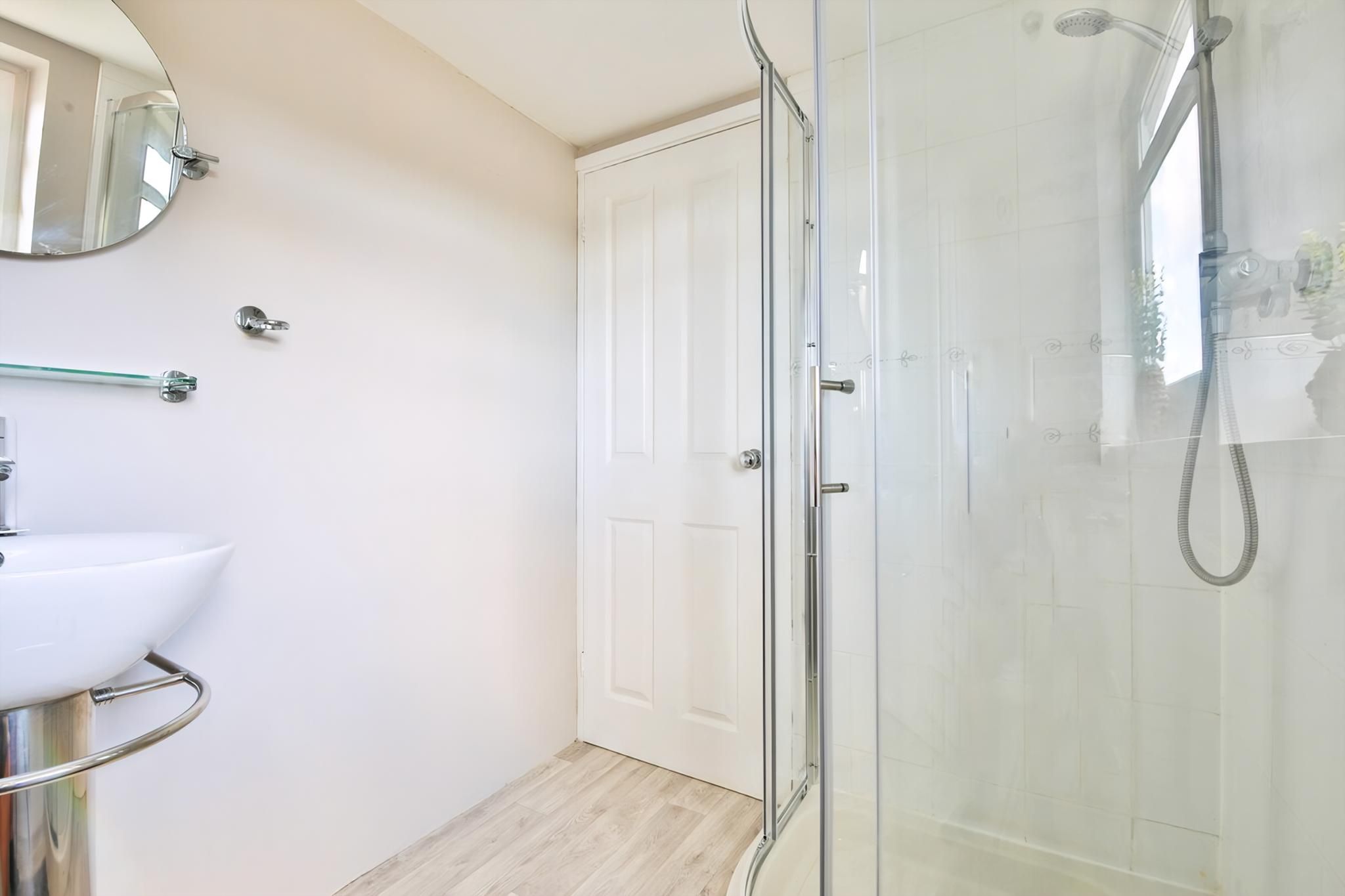 A bathroom with a glass shower enclosure, a white sink, and a mirror.