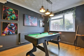 A pool table with a green felt surface, surrounded by walls with framed artwork, a window with blinds, and a ceiling with recessed lighting. - Spacious Three-bedroom Home With Pool Table (Cardiff)