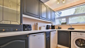 A compact kitchen with grey cabinets, a dishwasher, a washing machine, and a window with blinds.