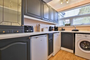 A compact kitchen with grey cabinets, a dishwasher, a washing machine, and a window with blinds.