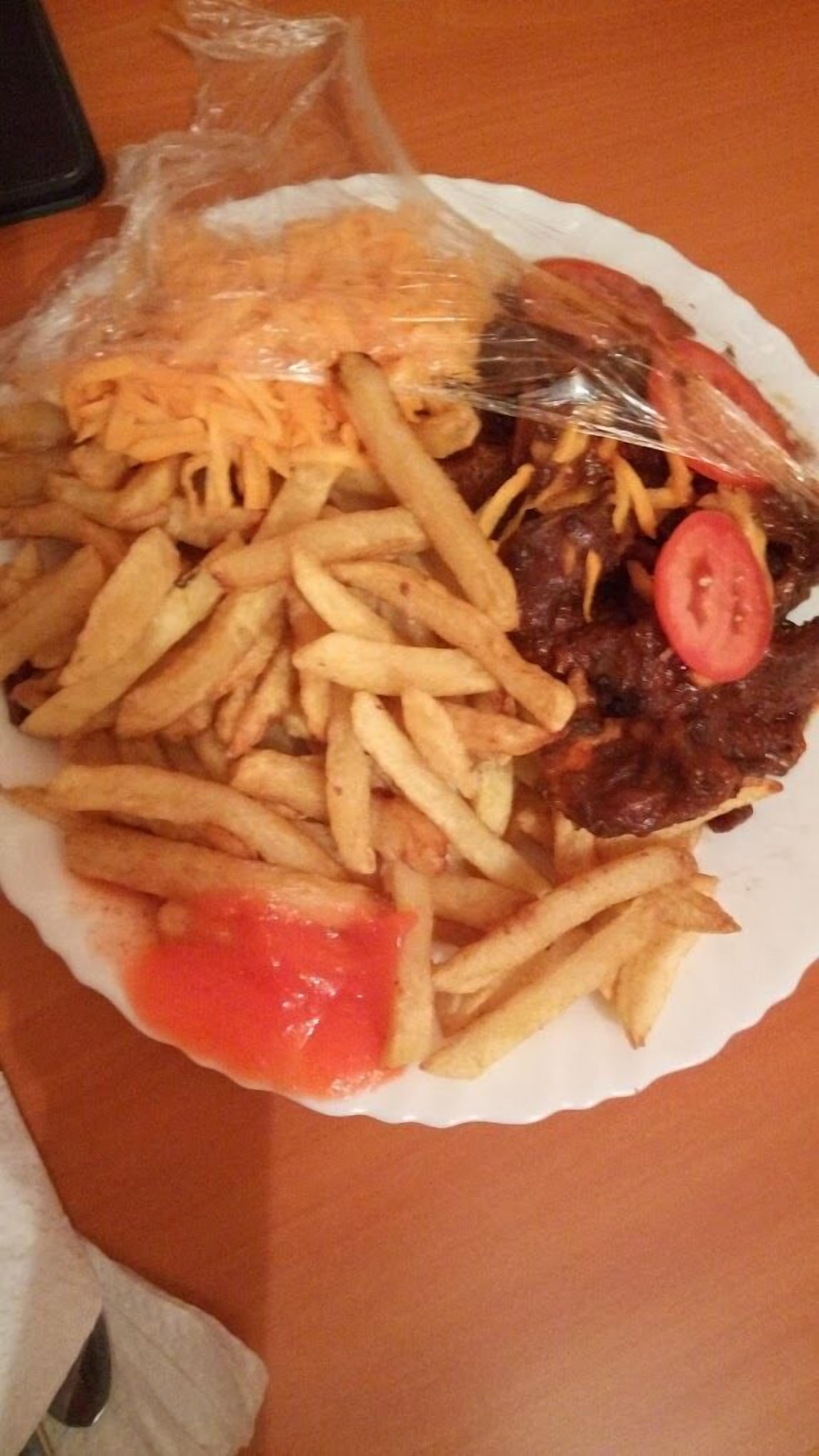 A plate of food with fries, a slice of tomato, and a bag of cheese.