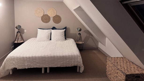 Een slaapkamer met een bed, twee bedlampen, een spiegel aan de muur en een geweven mand.