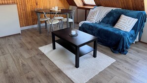 Een knus interieur met een houten plafond, een eettafel met stoelen, een blauwe bank en een tafeltje met een kaars.