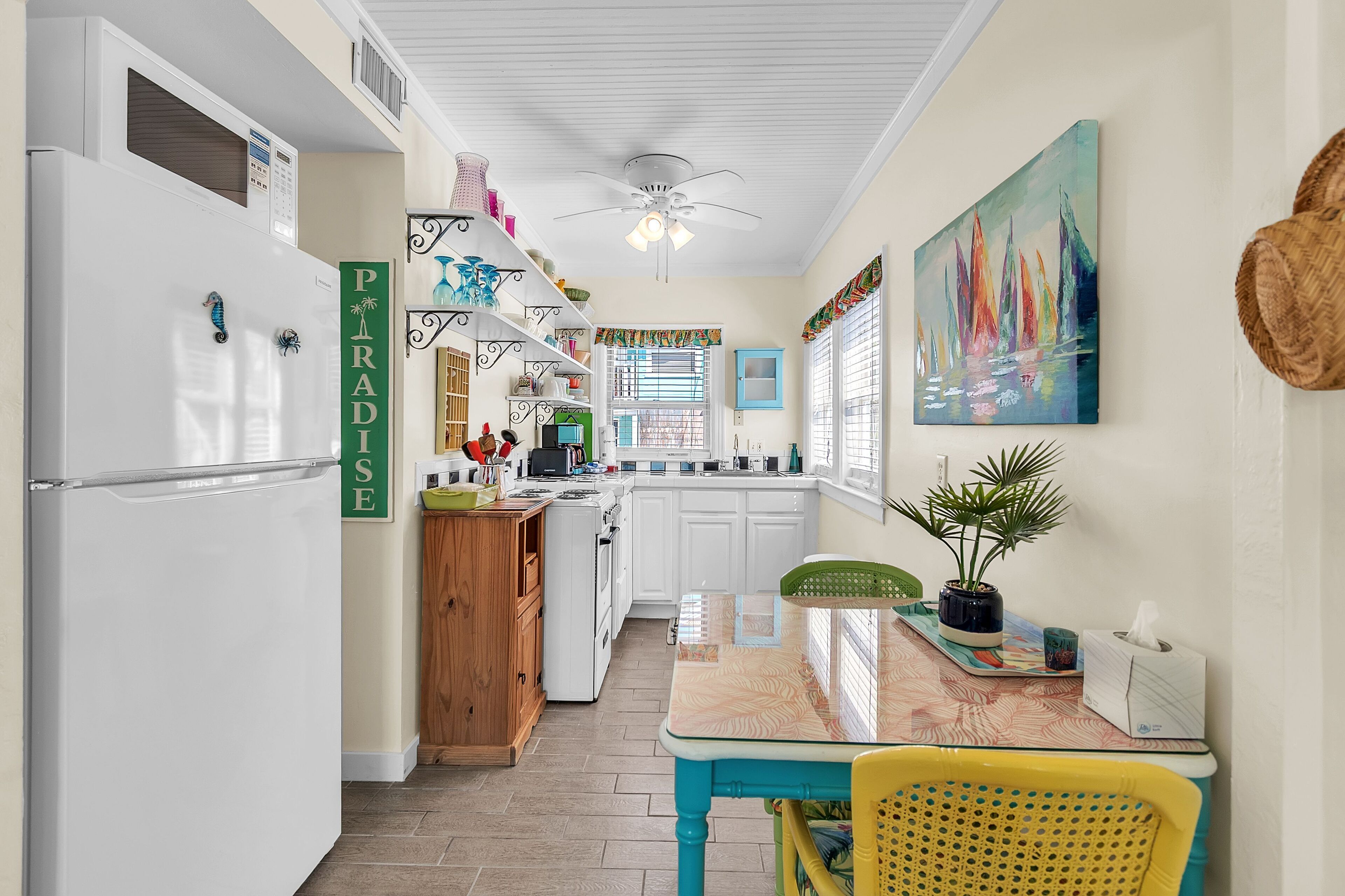 A kitchen with white cabinets, a refrigerator, a dining table with chairs, and a ceiling fan.