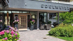 A modern building with a sign reading 'EDELWEISS' and a covered outdoor seating area with tables and chairs. - Hotel Edelweiss (Gerlos)