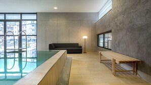 A modern indoor pool area with a sofa and a bench, large windows, and a lamp. - Hotel Edelweiss (Gerlos)