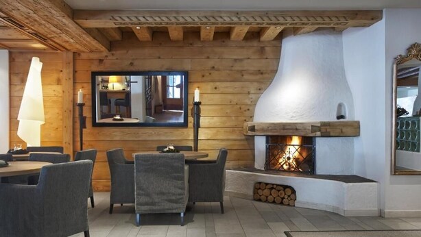 A cozy room with a fireplace, wooden walls, and a dining area with chairs and a table. - Hotel Edelweiss (Gerlos)