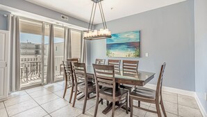 A dining area with a glass table and chairs, a painting on the wall, and a view through the glass door. - Ocean View l 5BR l Pool l Sleeps 16 l Luxury Villa (N. Myrtle Beach)