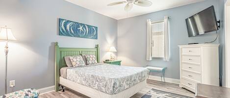A bedroom with a bed, a ceiling fan, a TV, a nightstand, a bench, and a dresser.