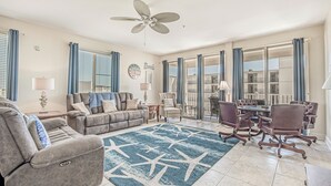 A spacious living room with a large ceiling fan, a dining area with a table and chairs, and large windows with curtains. - Ocean View l 5BR l Pool l Sleeps 16 l Luxury Villa (N. Myrtle Beach)