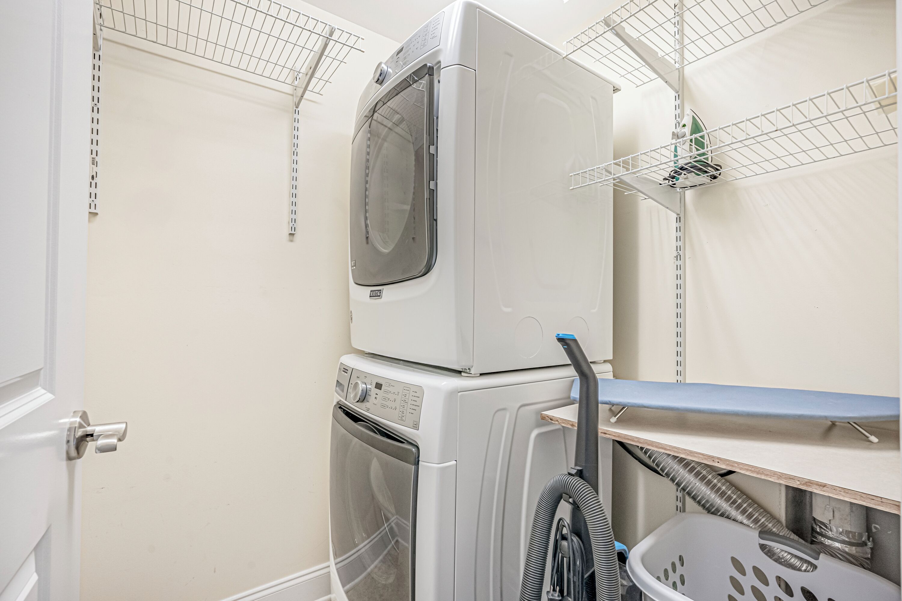 A laundry area with stacked washers and dryers, a metal drying rack, and a basket.