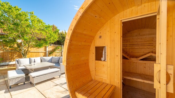 Un sauna en bois, doté d’un banc et d’une table, entouré de mobilier d’extérieur.