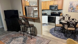 A modern kitchen with wooden cabinets, stainless steel appliances, and a dining area with a round table and chairs. - Complete Remodel 1 Block From the River Center, Minutes to LSU (Baton Rouge)
