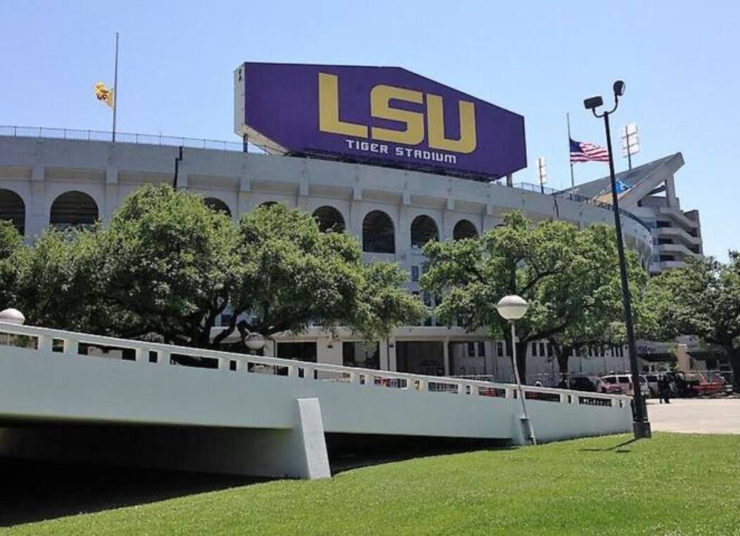 LSU Tiger Stadium with a prominent sign, a white bridge, and trees in the foreground.