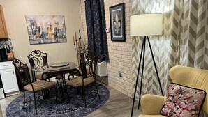 A dining area with a round table, chairs, and a blue rug. There is a lamp, a chair with a floral pillow, and a framed picture on the wall. - Complete Remodel 1 Block From the River Center, Minutes to LSU (Baton Rouge)