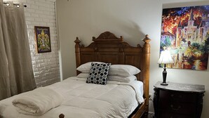 A neatly made bed with a wooden headboard, a patterned pillow, and a bedside table with a lamp. - Complete Remodel 1 Block From the River Center, Minutes to LSU (Baton Rouge)